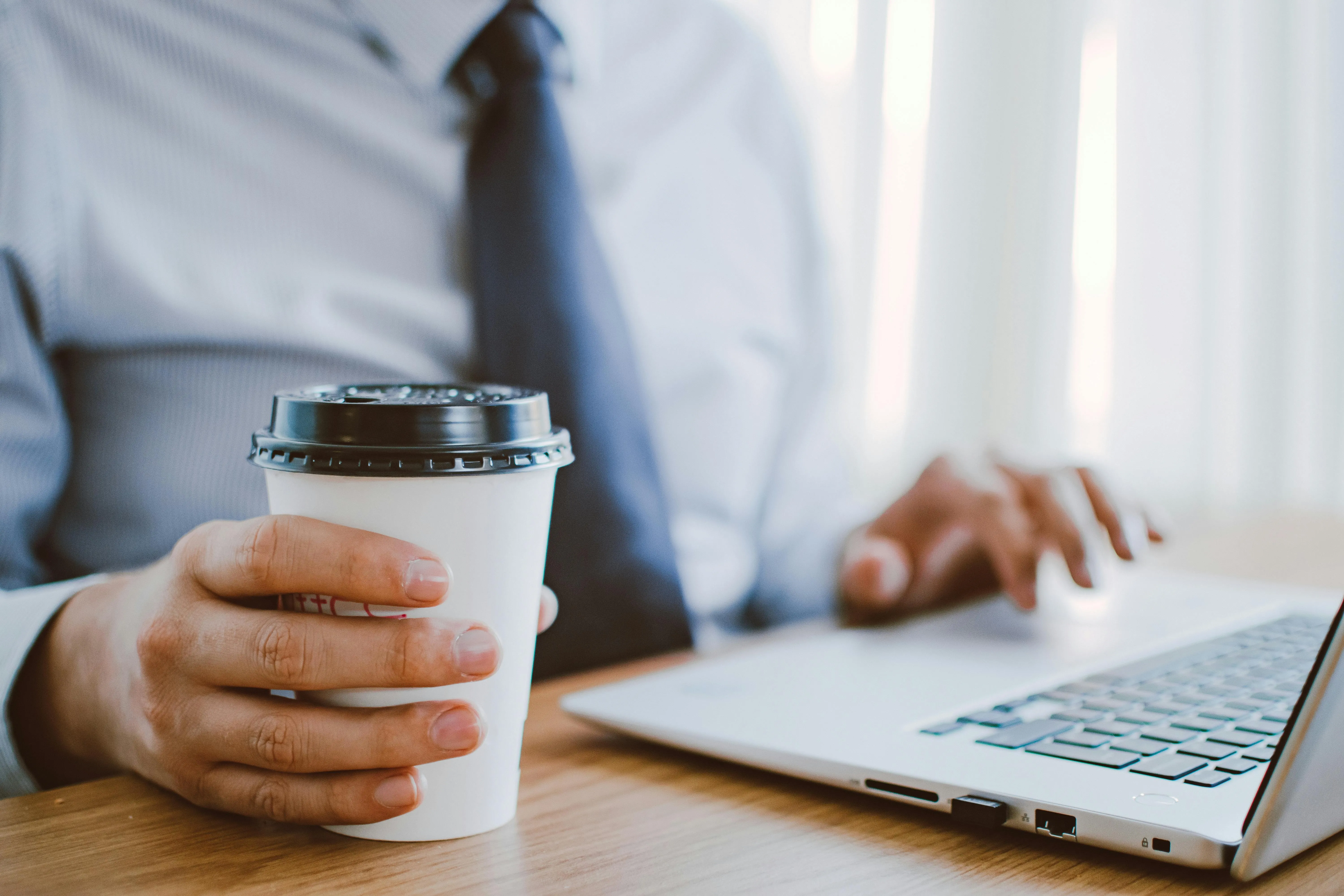 A person using his laptop while holding a coffee